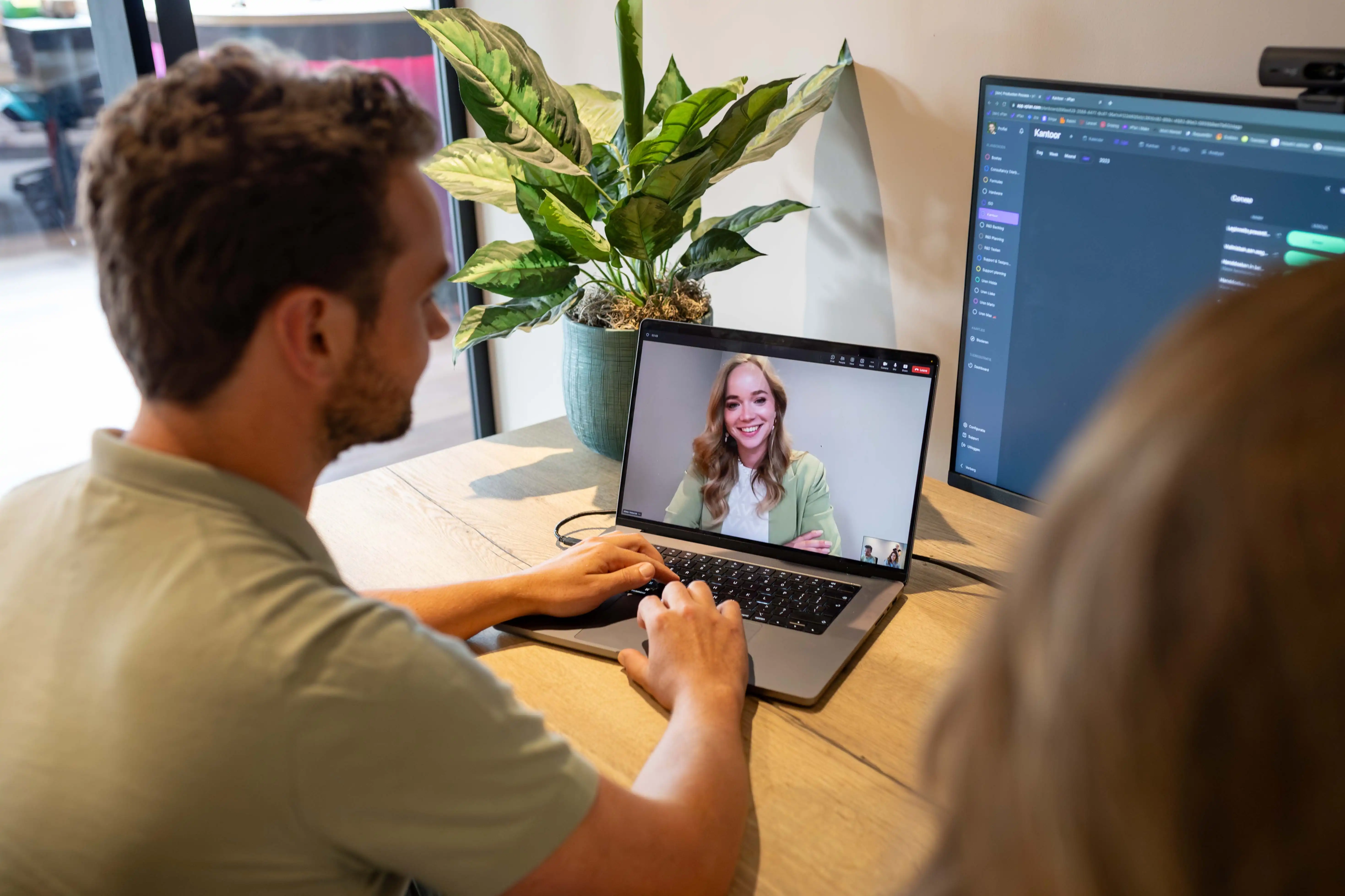 Een man die aan het videobellen is op zijn laptop met een vrouwelijke collega. Op het andere scherm ernaast zie je de planning tool vPlan.